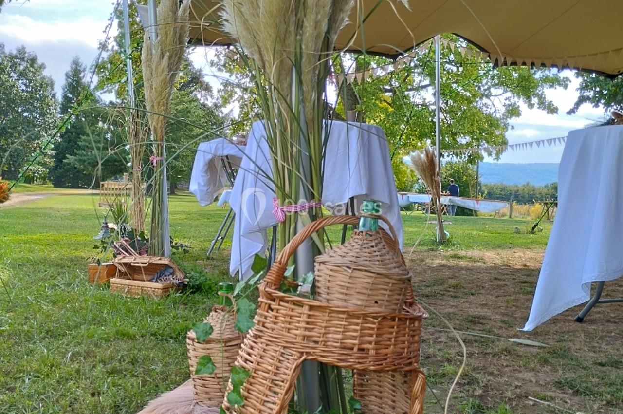 Décoration champêtre avec panier en osier, plantes vertes et herbes de la pampa sous une tente en plein air.