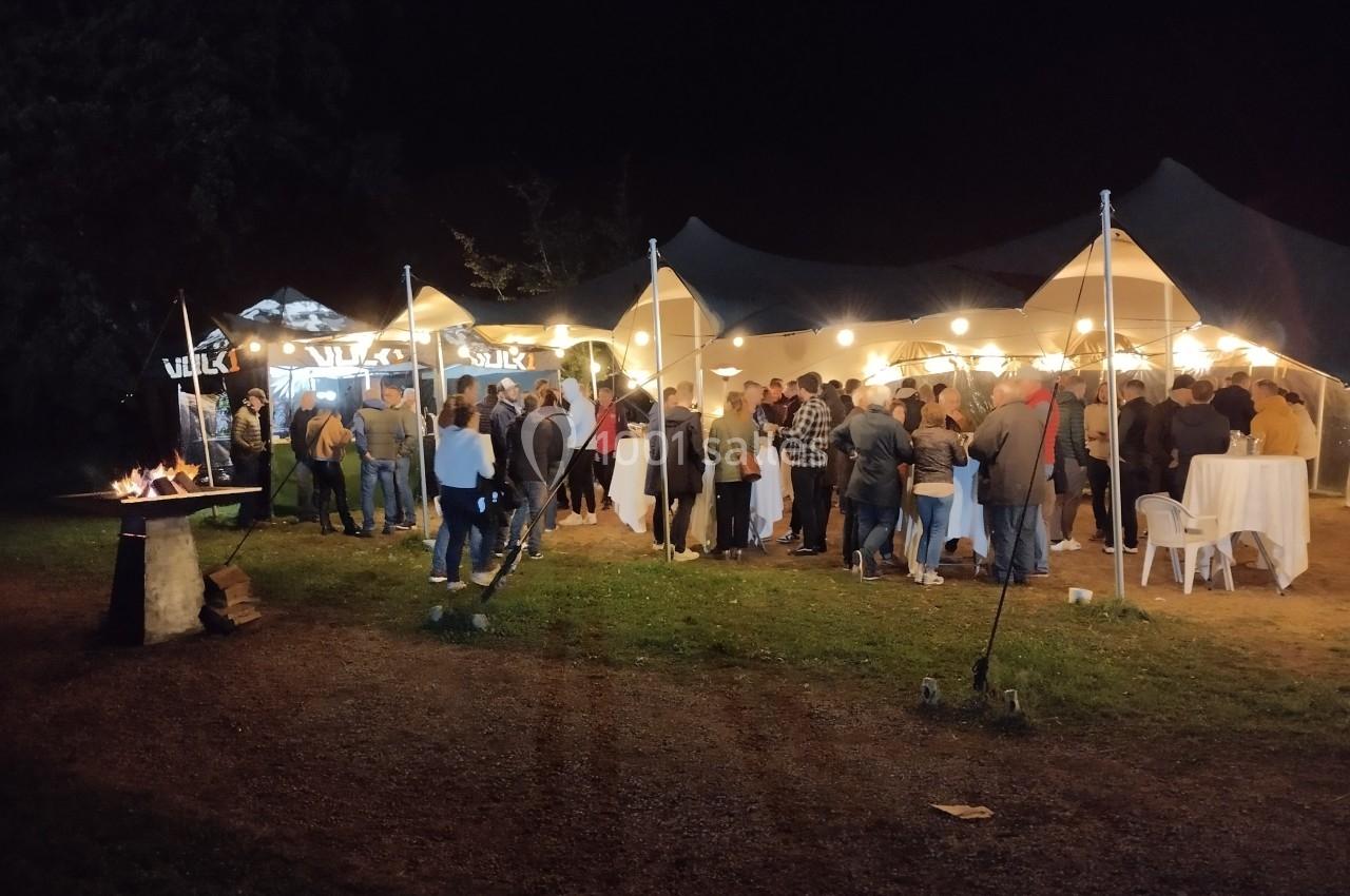 Groupe de personnes rassemblées sous des tentes éclairées en soirée, avec un brasero allumé à gauche.