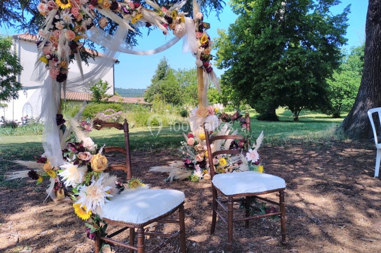 Deux chaises décorées de fleurs sous une arche florale dans un jardin ensoleillé.