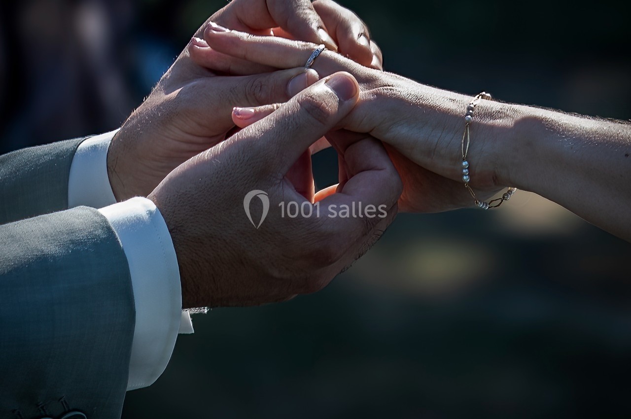 Un homme en costume glisse une alliance au doigt d'une femme dans un cadre sombre et intime.
