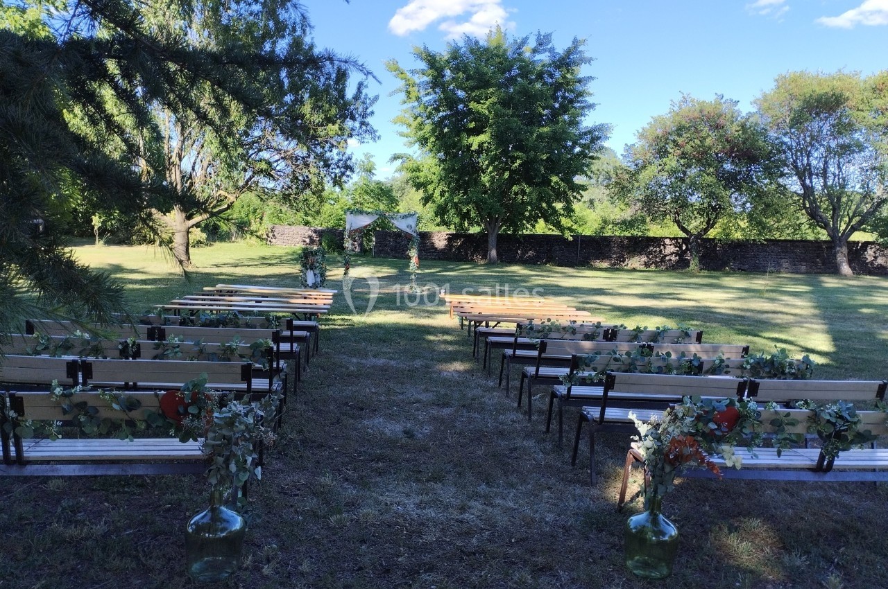 Allée centrale bordée de bancs décorés de feuillages, menant à une arche de mariage dans un jardin verdoyant.