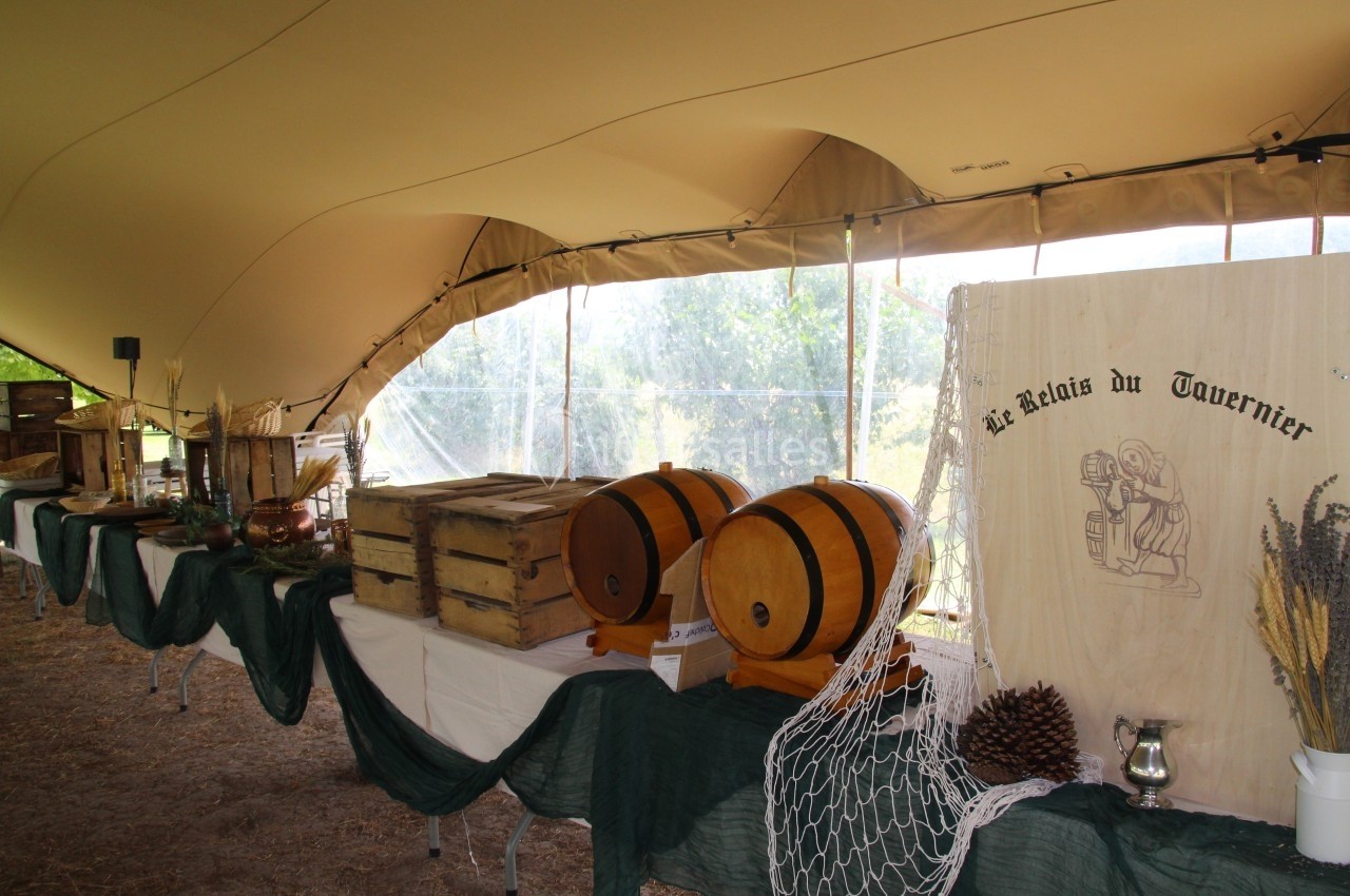 Buffet rustique sous une tente, avec tonneaux en bois, caisses en bois, décorations naturelles et panneau en bois gravé.