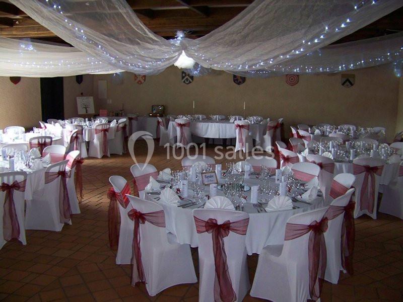 Salle de réception décorée avec des tables rondes, nappes blanches, chaises ornées de nœuds roses et voilages lumineux au…