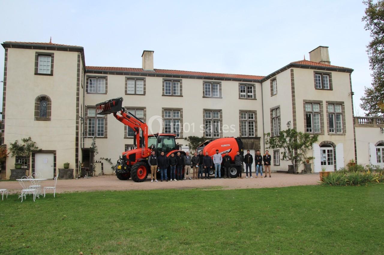 Un groupe de personnes pose devant un tracteur rouge et une machine agricole, devant un grand bâtiment ancien.