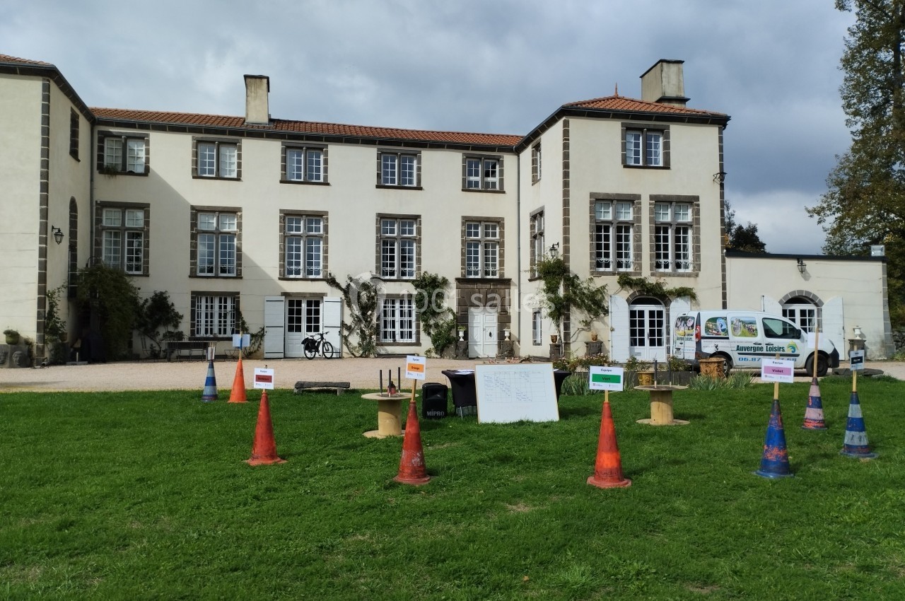 Location salle Sayat (Puy-de-Dôme) - Château de Féligonde #11 Façade d'un grand bâtiment ancien avec des cônes et panneaux colorés disposés sur une pelouse au premier plan.