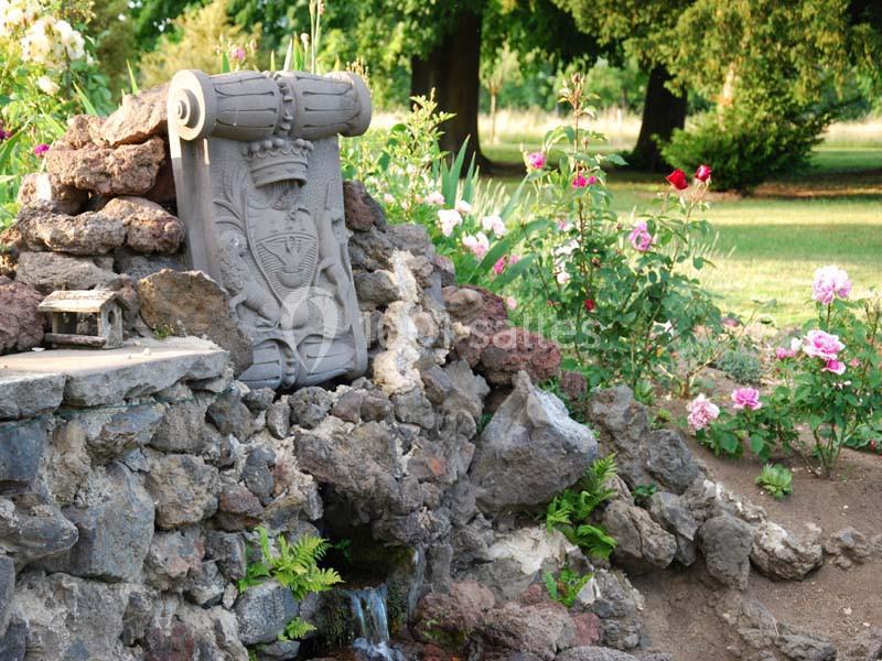 Statue décorative en pierre entourée de rochers, fleurs colorées et verdure dans un jardin.