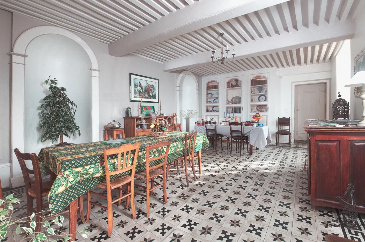 Salle à manger lumineuse avec tables couvertes de nappes colorées, chaises en bois et sol en carreaux de ciment.
