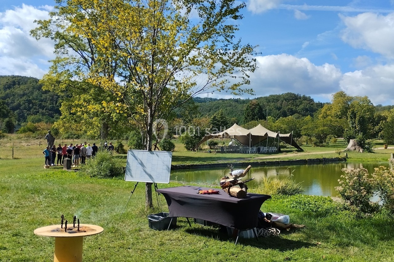 Kolanta Un espace extérieur avec une table dressée près d'un étang, des arbres et un groupe de personnes au loin.