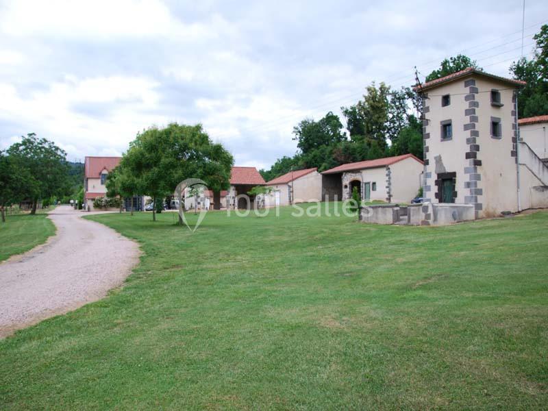Chemin en gravier menant à des bâtiments ruraux entourés de pelouses et d'arbres sous un ciel nuageux.