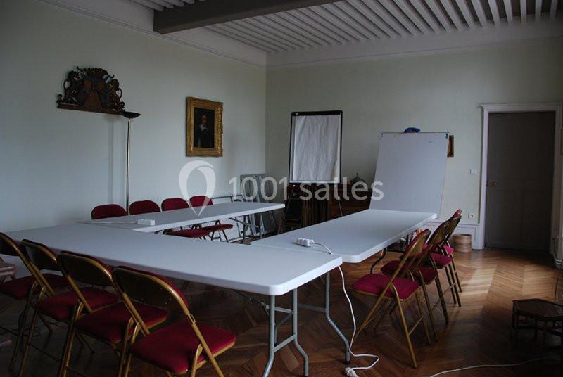 Salle de réunion avec tables blanches en U, chaises rouges, tableau blanc et parquet en bois.