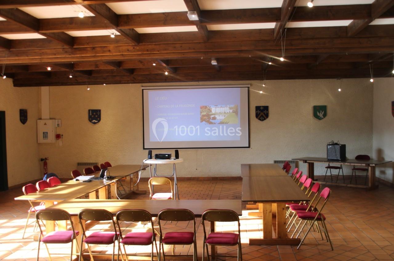 Salle de réunion lumineuse avec tables en U, chaises rouges, projecteur et écran affichant une présentation.