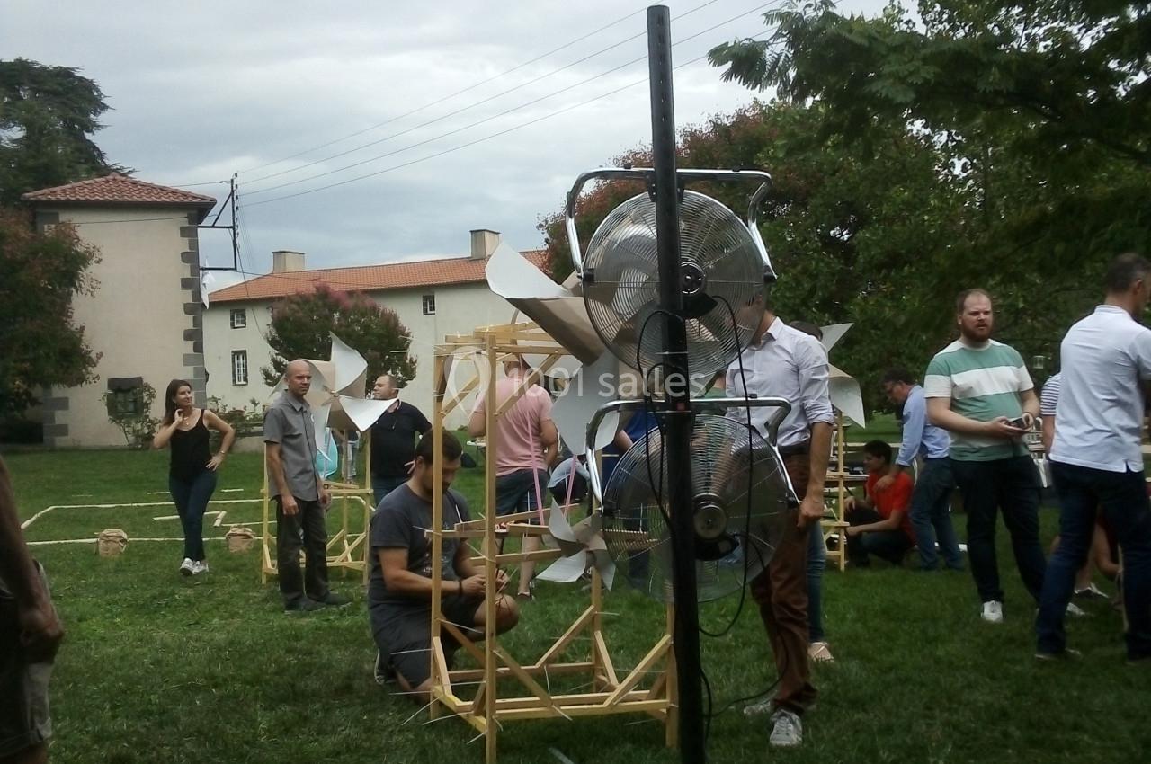 Des personnes assemblent des structures en bois et des ventilateurs dans un espace extérieur verdoyant.