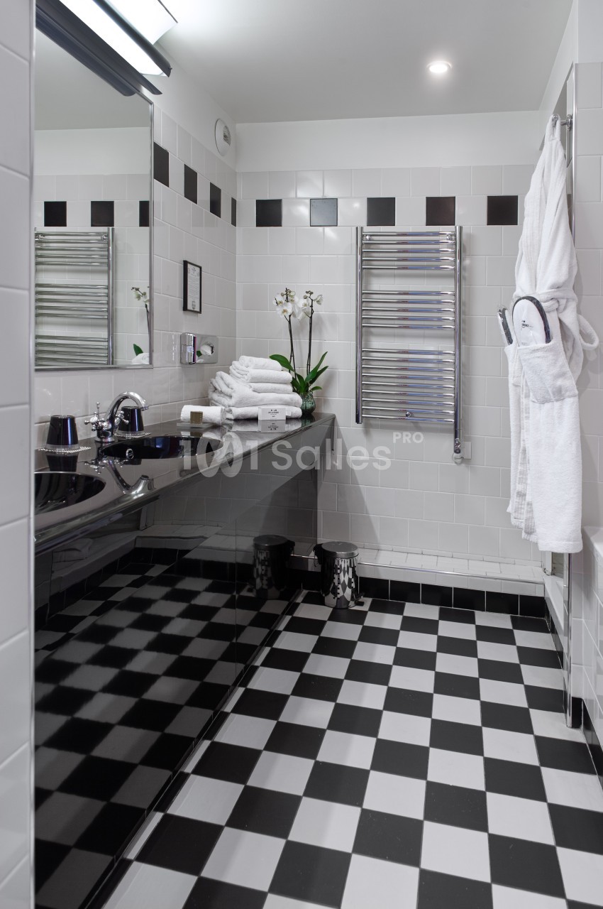 Salle de bain moderne avec carrelage noir et blanc, lavabo, miroir, porte-serviettes chauffant et orchidée blanche.
