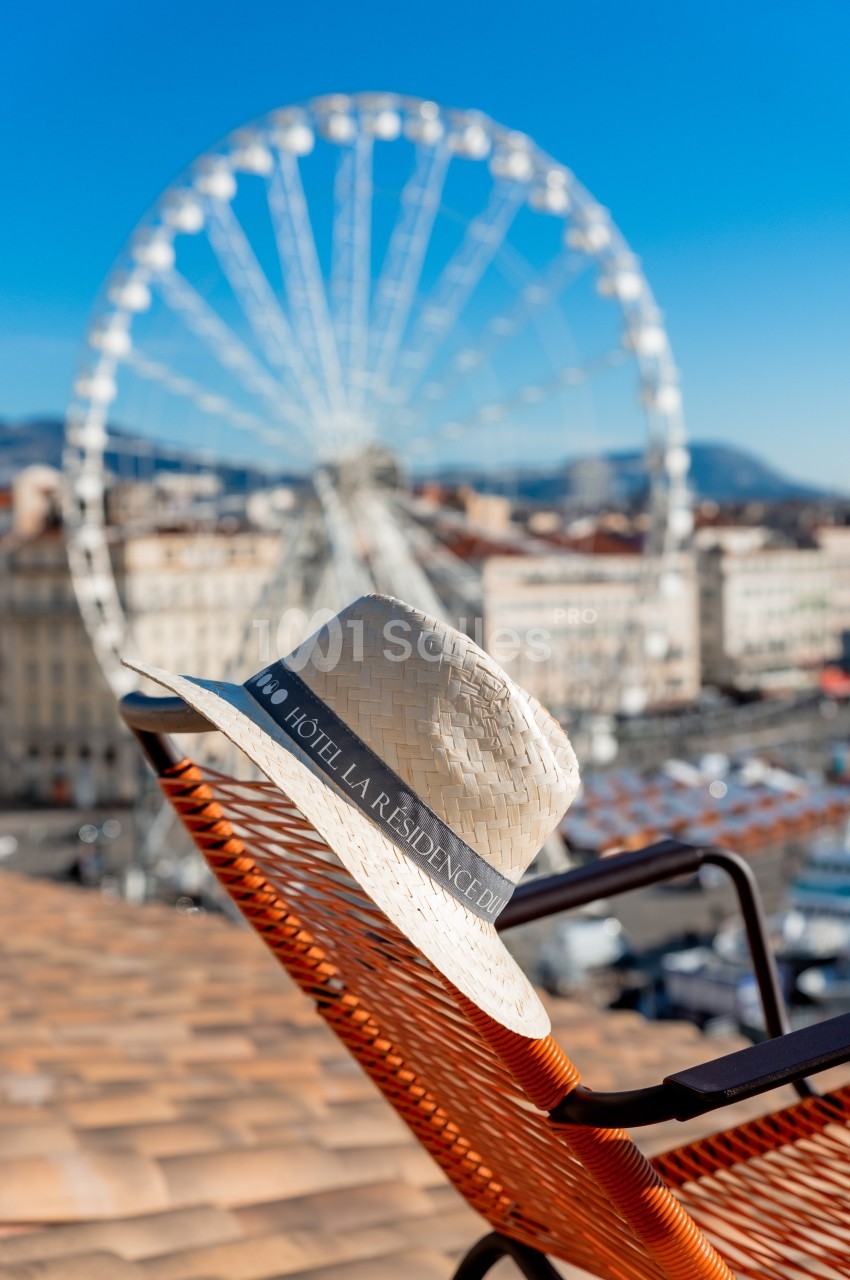 Chapeau en paille marqué ’Hôtel La Résidence’ posé sur une chaise, avec une grande roue en arrière-plan.