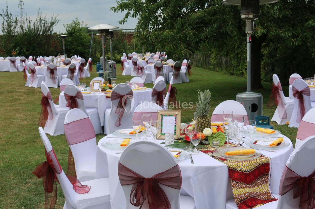 Tables rondes décorées avec nappes blanches et rubans rouges, disposées en extérieur pour un événement festif.