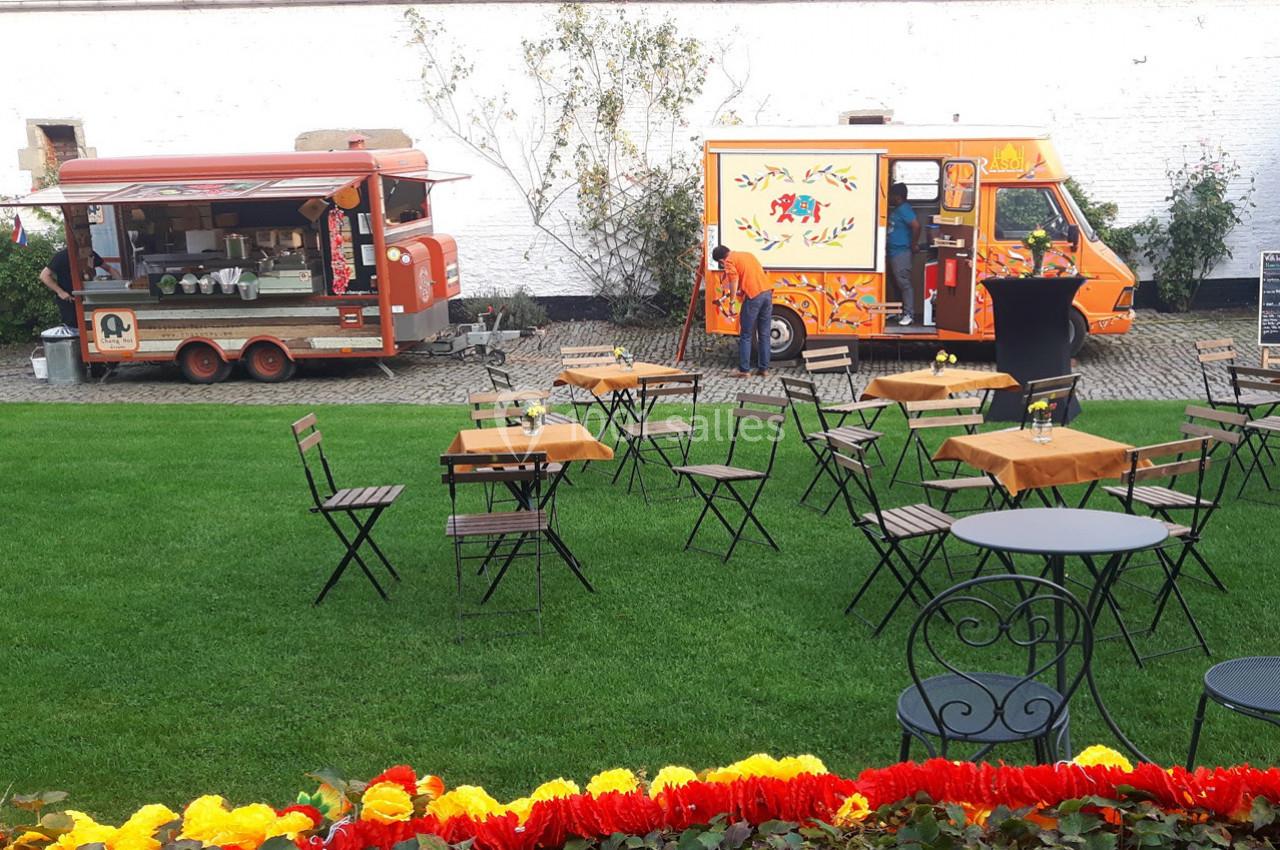 Deux food trucks colorés stationnés près d'un espace vert avec des tables et chaises en plein air.
