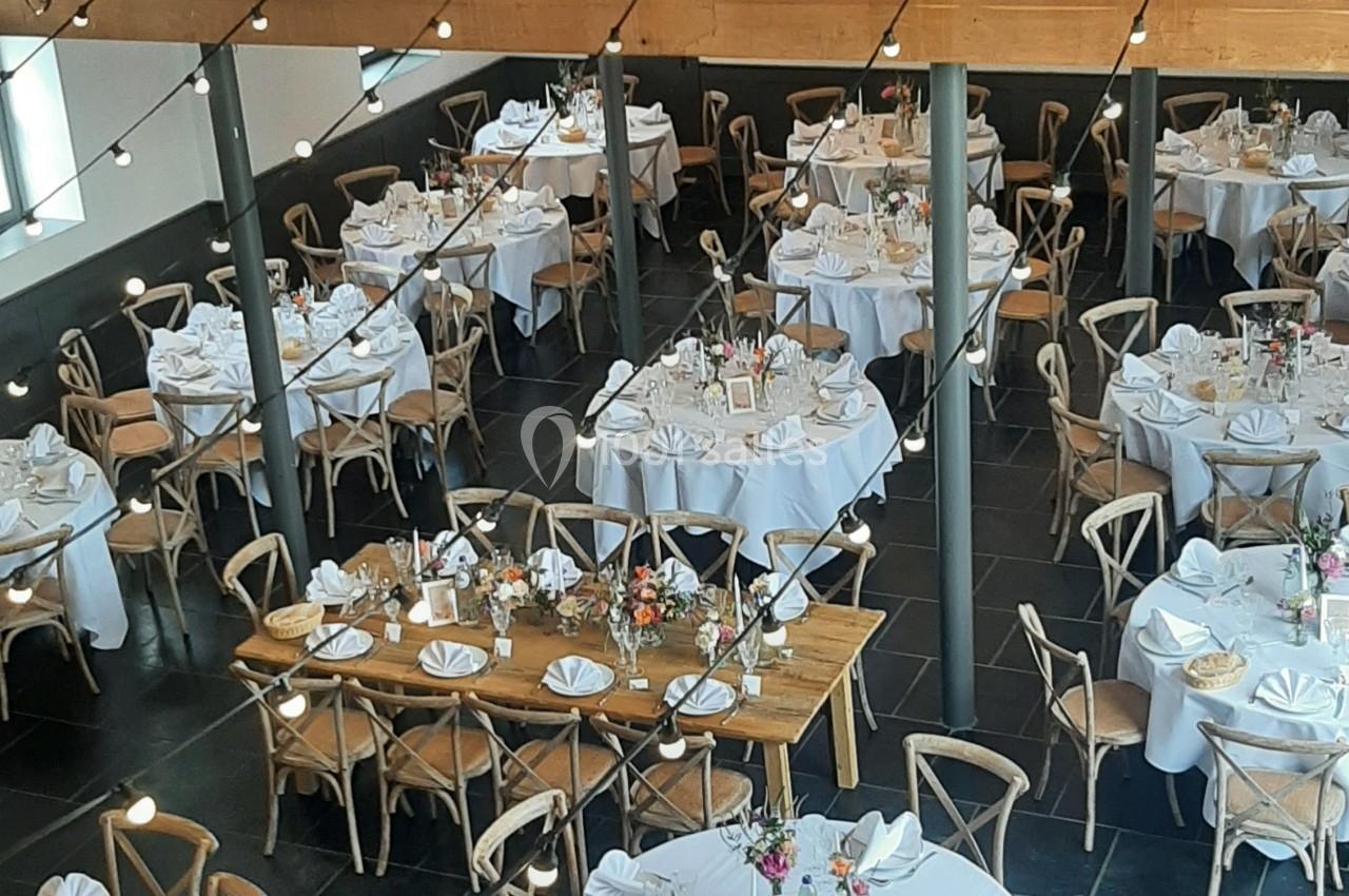 Salle de réception élégante avec tables rondes et rectangulaires dressées, décorée de fleurs et éclairée par une boule…