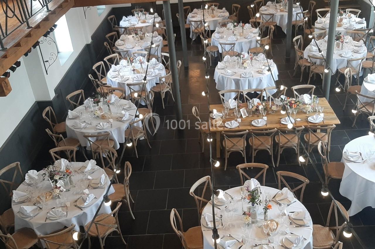 Salle de réception avec tables rondes et rectangulaires dressées, nappes blanches et décorations florales.