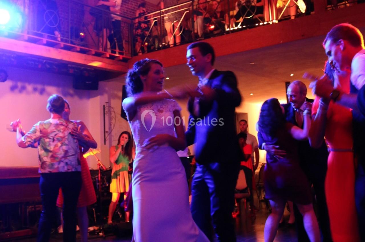 Un couple danse au centre d'une salle de réception éclairée, entouré d'invités sur la piste et à l'étage.