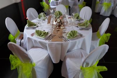 Table de réception décorée avec nappes blanches, serviettes vertes pliées, chaises ornées de nœuds verts et centre de table…