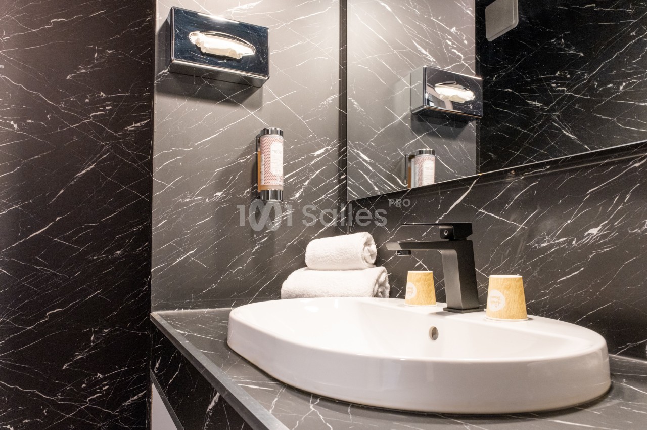 Lavabo moderne avec robinet noir, serviettes roulées et gobelets posés sur un plan en marbre noir veiné.