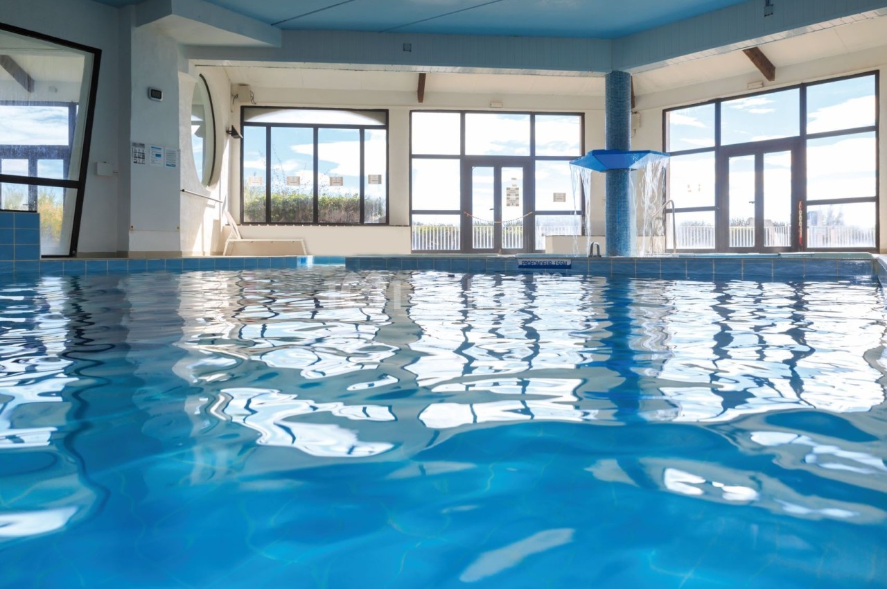Piscine intérieure avec eau claire, entourée de grandes baies vitrées laissant entrer la lumière naturelle.