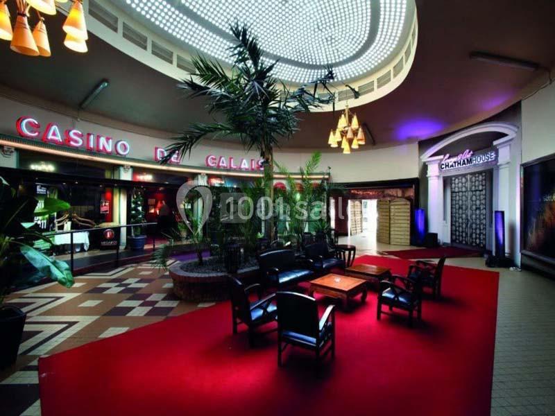 Espace intérieur avec fauteuils noirs, tapis rouge, plantes et enseignes lumineuses du Casino de Calais.