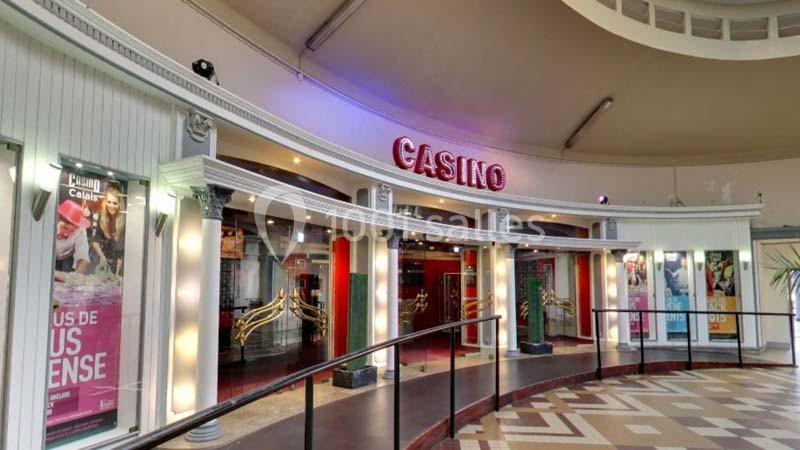 Façade d'un casino avec enseigne lumineuse rouge, entourée de colonnes blanches et d'affiches publicitaires.