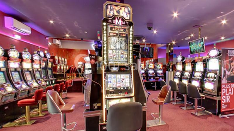 Salle de jeux avec plusieurs machines à sous alignées, éclairage tamisé et fauteuils disposés devant les machines.