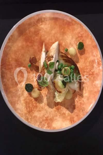 Assiette gastronomique avec filet de volaille, purée, légumes verts et décorations sur une assiette orange.