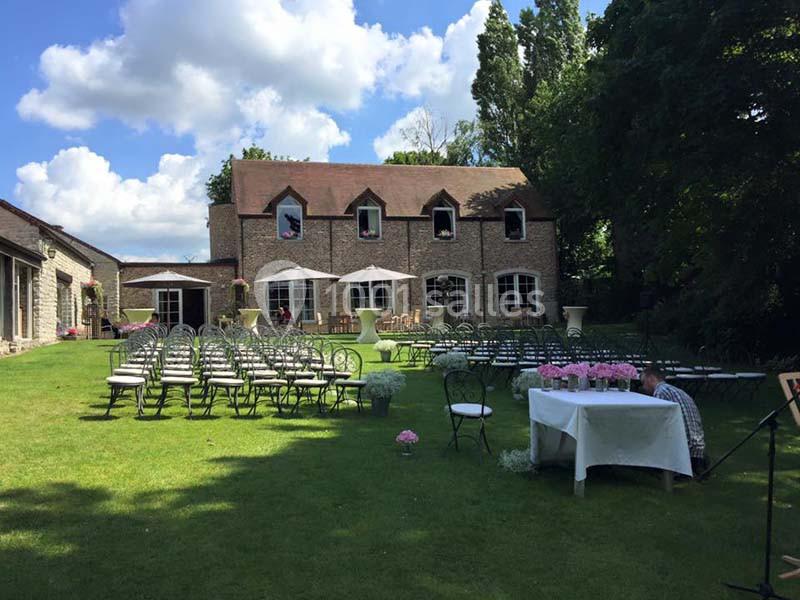 Chaises disposées en rangées sur une pelouse devant une maison en pierre, préparées pour un événement en plein air.