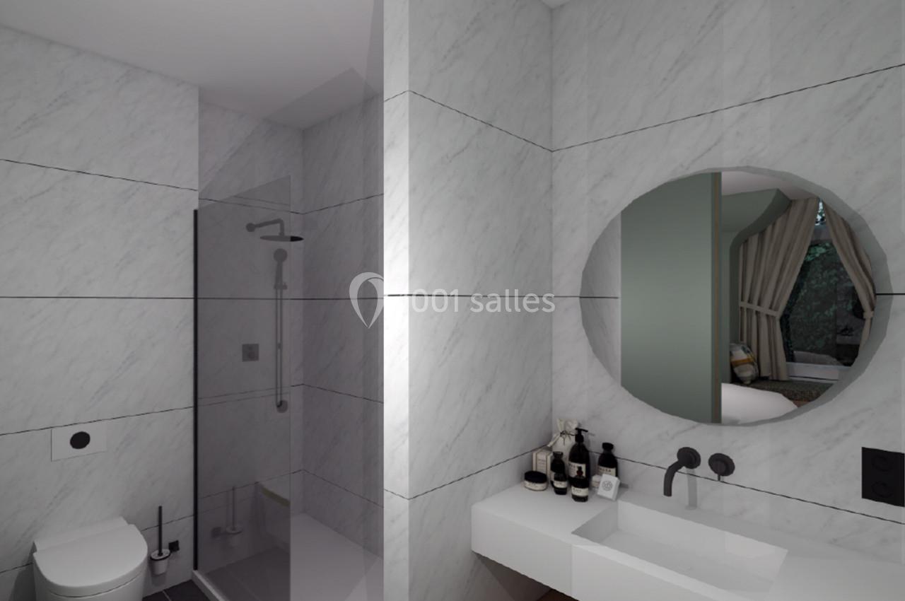 Salle de bain moderne avec murs en marbre, douche vitrée, lavabo blanc, miroir rond et accessoires de toilette.