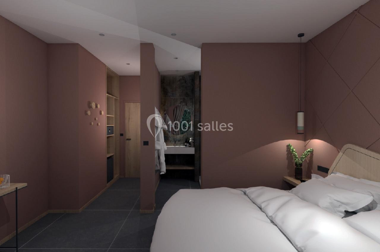 Chambre moderne avec murs roses, lit double, éclairage doux, et salle de bain attenante visible en arrière-plan.