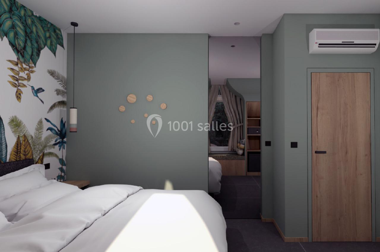 Chambre moderne avec lit, mur vert décoré, papier peint tropical, et vue sur un coin cuisine avec fenêtre.