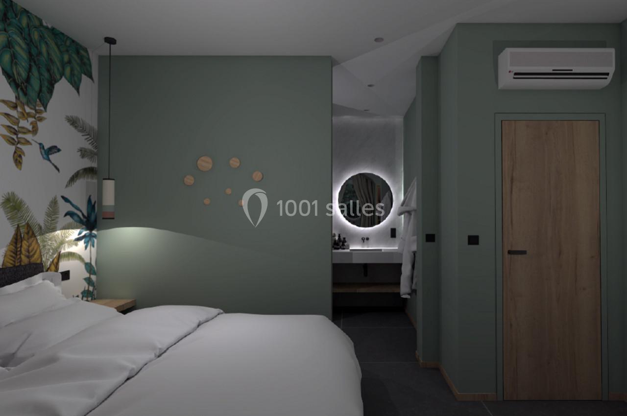 Chambre moderne avec mur vert, lit, éclairage doux, et vue sur une salle de bain avec miroir rond éclairé.