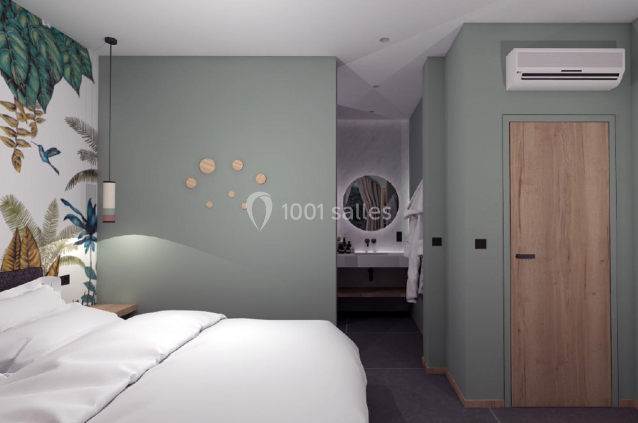 Chambre moderne avec lit, mur vert décoré, papier peint tropical et vue sur une salle de bain avec miroir rond.