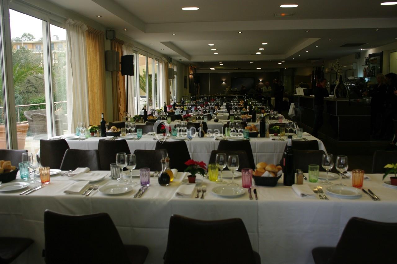 Salle de réception avec tables dressées, nappes blanches, verres colorés et couverts, prête pour un événement.