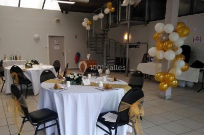 Salle décorée pour un événement avec tables alignées, nappes blanches, compositions florales et allée centrale ornée.