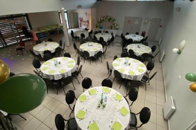 Salle décorée pour un événement avec tables alignées, nappes blanches, compositions florales et allée centrale ornée.