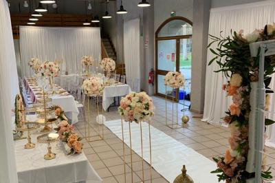 Salle décorée pour un événement avec tables alignées, nappes blanches, compositions florales et allée centrale ornée.