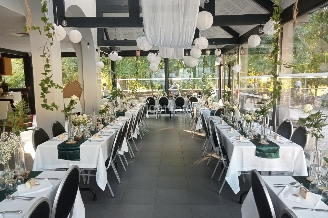 Salle de réception décorée pour un événement, avec tables dressées, nappes blanches et ornements floraux.
