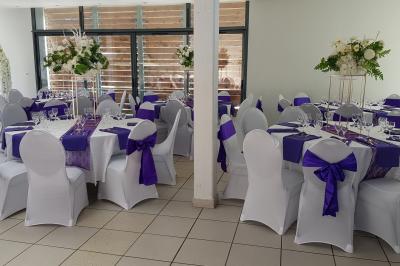 Salle décorée pour un événement avec tables alignées, nappes blanches, compositions florales et allée centrale ornée.