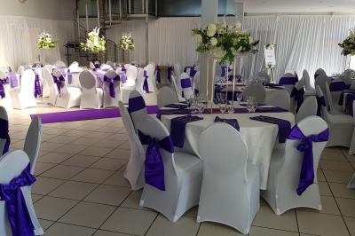 Salle décorée pour un événement avec tables alignées, nappes blanches, compositions florales et allée centrale ornée.