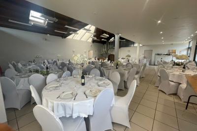 Salle décorée pour un événement avec tables alignées, nappes blanches, compositions florales et allée centrale ornée.