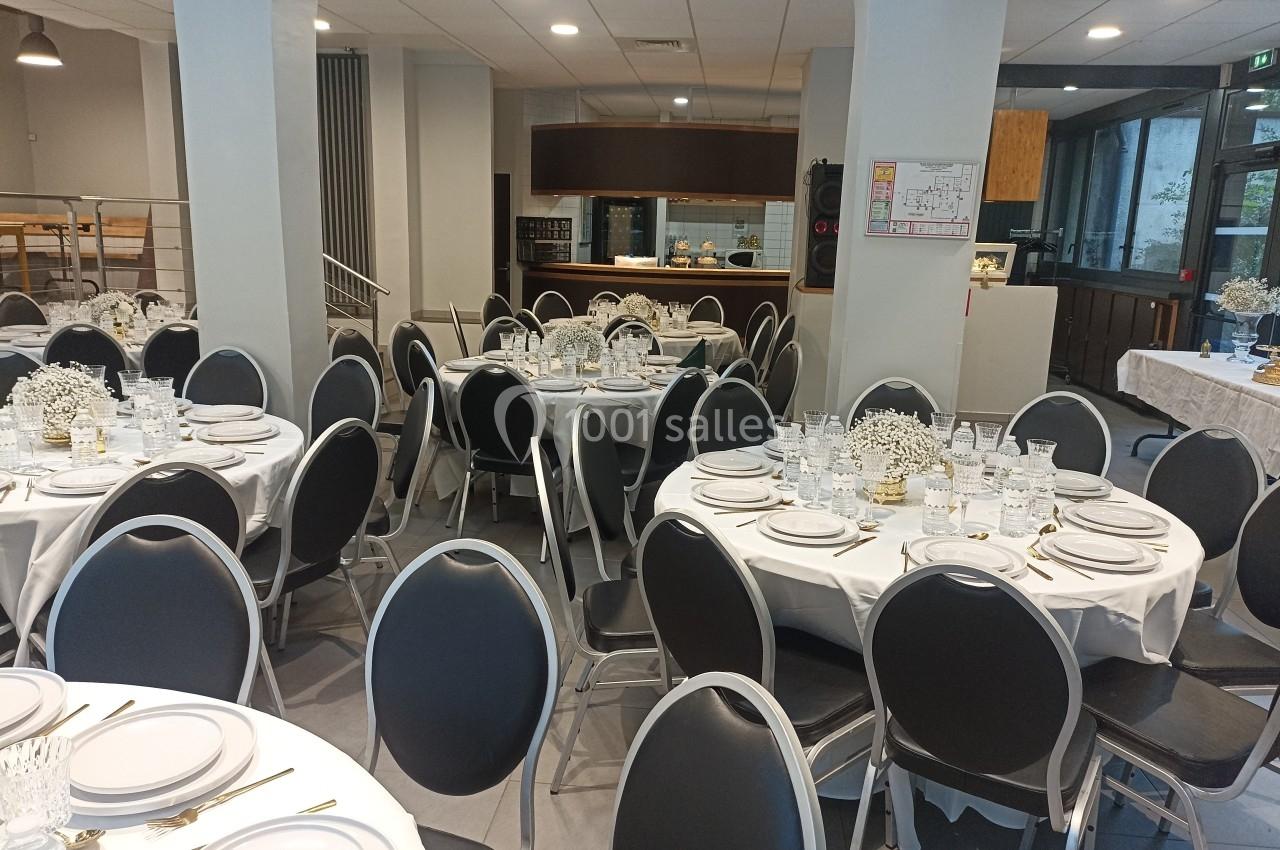 Salle de réception avec tables rondes dressées, nappes blanches, vaisselle élégante et décoration florale discrète.