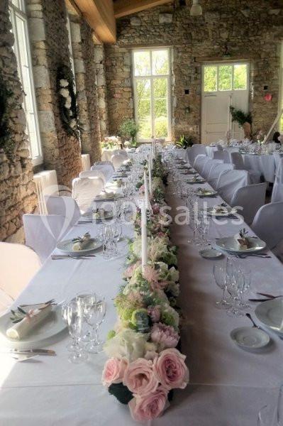 Salle en pierre avec une longue table dressée, ornée d'une décoration florale centrale et de vaisselle élégante.