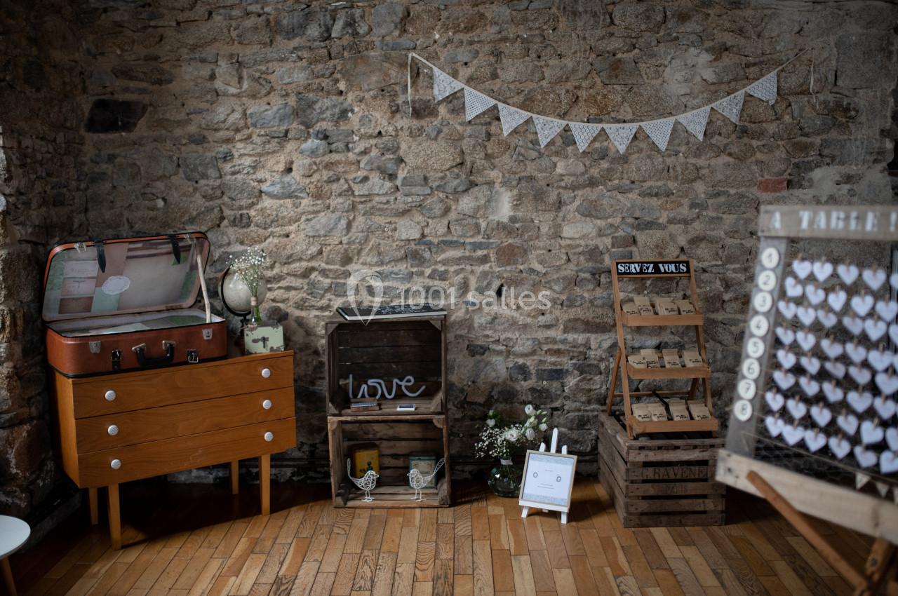 Décoration de mariage vintage avec valise, caisses en bois, guirlande et présentoirs sur un mur en pierre.