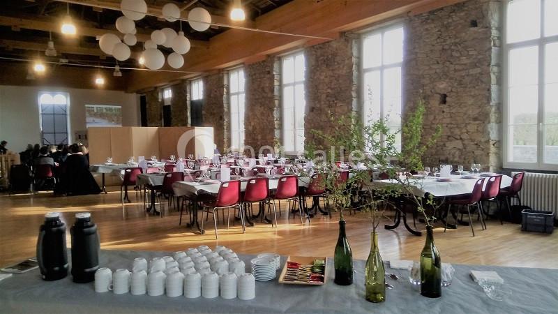 Salle de réception lumineuse avec tables dressées, chaises rouges et buffet en premier plan.