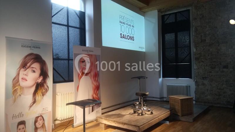 Salle de présentation avec affiches de coiffure, écran projetant un message et chaise au centre.