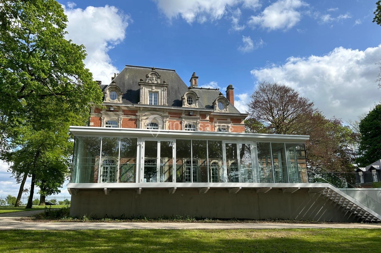 Façade d'un bâtiment ancien en briques rouges avec une extension moderne vitrée, entouré de verdure et d'arbres.